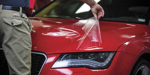 Installer applying protective film to a red car hood